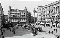 Stureplan före år 1918 med Hôtel Anglais och myllrande folkliv, spårvagnar linje 3 och 5, hästkärror, cyklande och gående människor i halmhatt.