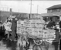 Man lastar en vagn med grönsakslådor. I bakrunden skylten Klarahallen med Normas servering (1933-1962). Klara strand