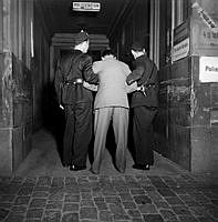 Två polismän med en gripen man vid polisstationen Mäster Samuelsgatan 59. Mannen gripen i samband med kravaller vid Berzelii Park den 21 juli 1951.