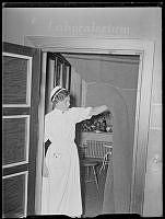 Sjuksköterska med Sofiasystermössa  håller undan en mörkläggningsfilt vid ett laboratorium.