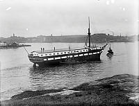 Fregatten HMS Vanadis sista resa. Utanför Kastellholmen och med Beckholmen till vänster och Fåfängan synlig i bakgrunden. Två bogserbåtar hjälper till.