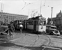 Trafik och folkliv på Norrbro. Bilar, lastbilar, spårvagnar och cyklister. Till vänster Stockholms slott. Till höger Riksdagshuset.