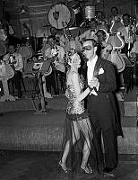 Dansande par med ögonmasker framför dansorkestern vid maskerad på restaurang och nöjesetablissemanget Fenix-Kronprinsen.