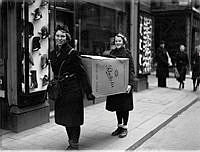 Två unga kvinnor bär en stor pappkartong med kläder till klädinsamlingen till Finlands folk.