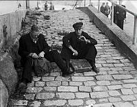 I samband med inkallelse för mobilisering efter andra världskrigets utbrott sitter två män och äter smörgås på en trottoar.
