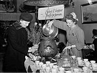 Kvinna och kafébiträde vid uppdukat kaffebord med kaffekoppar och kaffesamovar. Man tvingades begränsa påtårerna under krigsårens kafferansonering.