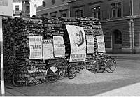 Vedstapel med valaffischer från Arbetarepartiet socialdemokraterna och Högern, samt en affisch från Gröna Lund.