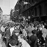 Fredsdagen den 7.e maj 1945 på Kungsgatan i Stockholm. 
Glada folkmassor längs gatan och från husfasadernas fönster kastar människor papper och girlanger.