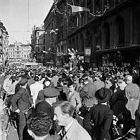 Fredsdagen den 7.e maj 1945 på Kungsgatan i Stockholm. 
Glada folkmassor längs gatan och från husfasadernas fönster kastar människor papper och girlanger.