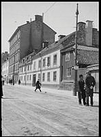 En polis med kask och sabel samtalar med en man. Skånegatan västerut från Nytorgsgatan. Skånegatan 19, 17 och 15. Nu Skånegatan 75-73.