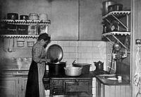 Interiör från köket på Katarina västra barnkrubba med en kokerska som står vid vedspisen och lagar mat.