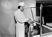 Kvinna på Mjölkcentralen mäter upp mjölk i en mjölkkanna med ett så kallat långskaft.