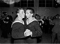 Två män i sjömansuniform dansar med varandra vid en fest på en skärgårdsförläggning under beredskapstiden för andra världskriget.