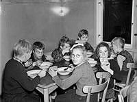 Barn runt bord i skolbespisningen äter soppa och smörgås.