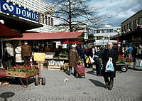 Vy längs Farta Torg med människor, torghandel och blommor.