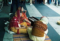 Tre stycken Hare Krishna medlemmar sjunger och spelar lovsånger på trottoaren utanför Åhlénsvaruhuset på Drottninggatan.