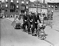Snabb trio på en trepersoners tandemcykel cykel på Riksbron: Nils Nilsson,  Axel Svensson och Per Libert. I fonden Strömgatan med  Adelswärdska huset, Sagerska huset och Arvfurstens palats.

