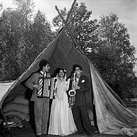 Under ett tälttak uppträder två manliga musiker och en kvinna vid ett romskt bröllop.