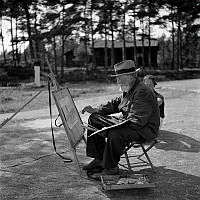 Reportage från Sandhamn under sandhamnsregattan 1941. Den nordiska seglarfesten.
Med en fläkt från sol, sommar och Sandhamn. En äldre man sitter och målar vid sitt stativ.
