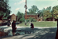 Djurgården. Orsakullen på Skansen sedd med Hackstugan, Kaplansloftet och härbre till Moragården. I mitten midsommarstång.