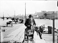 En skärslipare slipar knivar på en slipsten vid Munkbron. I fonden Slussen och Katarinaberget.