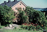 Dalarö tullhus sett bakom ridå av grönska. Längst t.h. syns innerskärgård.