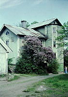 Dalarö. Äldre trävilla med korrugerat plåttak och trapphus. Lila syrén döljer fasaden i mitten.