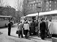 Köande går ombord på buss vid Jarlaplan. I bakgrunden kvarteren Roslagen och Muraren.