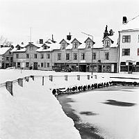 Vaxholm. Vy mot norr över kajen vid Söderhamnen och Söderhamnsplan mot trähusbebyggelse med butiker i bottenvåningen längs Hamngatan.