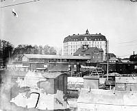 Vy från öster över Liljeholmen station och stationsområde med godsvagnar och en järnvägsarbetare. I fonden Gamla Stationshuset och det sju våningar höga Liljeholmens Municipalhus.