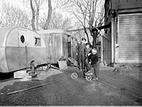 Tre barn leker med en trehjuling framför två husvagnar vid Lilla Tanto. I fonden skymtar Årstabron