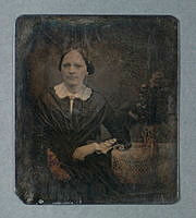 Porträtt av en kvinna som sitter vid ett litet bord med en blomvas. Daguerreotyp.