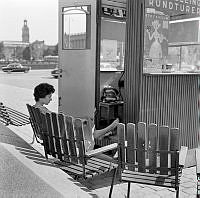 En flicka sitter i sommarskuggan bakom resebyrån på Gustav Adolfs torg. I fonden Storkyrkan.