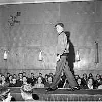 Mannekänguppvisning. I kårhuset på Holländargatan visar Stockholms högskolestudenter upp sitt vårmode 1958. Modellen Curt Dietmann visar kläder på scenen inför publik.