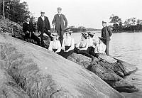 Stockholmare på Ekudden. Fem damer och fyra herrar på en klippa vid stranden.