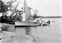 En liten segelbåt och en eka vid stranden. Ombord på segelbåten från vänster Anna Öhman, Maria Johansson och Aina Winborg. I ekan Hjalmar Öhman.