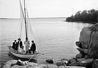 En segelbåt vid en strand med personer ombord.