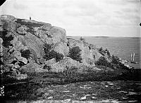 Skärgårdsvy med berg, klippor och en segelbåt.