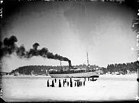 Finska Ångfartyget S/S Oihinna i Furusundsleden. Människor på isen väntar med båtar. Tullpersonal.