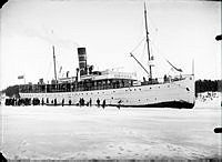 Finska Ångfartyget S/S Oihinna i Furusundsleden lastar och lossar. Människor på isen väntar med båtar.