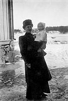 Maria Johansson står utanför ett hus med dottern Dagny (född 1908) på armen. Det är snö på marken.