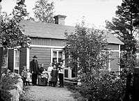 Gruppbild av två män och och en kvinna, sex barn och en katt, framför ett hus.