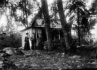 Två kvinnor och en man framför ett litet hus med veranda.