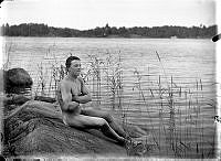Självporträtt av fotograf Otto Johansson, naken på en klippa vid stranden.