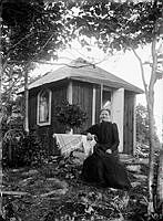 En kvinna sitter utanför ett litet hus. 