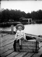 En flicka (kanske Dagny Johansson) sitter på en trälåda på en brygga.