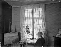 Konstnären och författaren Albert Engström sittande framför ett staffli med en Eugen Janssonmålning. På bordet ligger en Zorn-etsning.