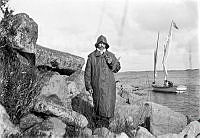 Fotografen Otto Johansson i oljerock och sydväst. I bakgrunden en liten segelbåt.