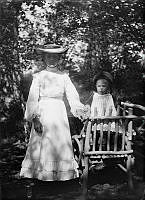 En kvinna med ett litet barn stående på en trädgårdsstol.