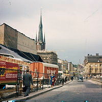 Klarabergsgatan sedd västerut vid blivande Sergels Torg. Till vänster reklam för Knäppupprevyn och turnévagn. I bakgrunden Klara kyrka.